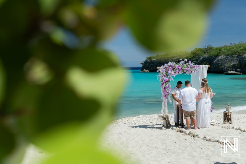 A Serene Beach Wedding Ceremony Taking Place on a Sunny Day With Guests, Floral Decorations, and Turquoise Waters in the Background Near a Picturesque Coastal Location