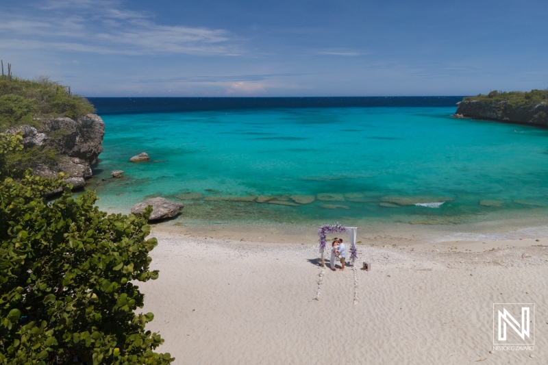 Beautiful Tropical Beach Scene Featuring a Wedding Setup Under a Floral Arch on the Shore, With Clear Turquoise Waters and a Bright Blue Sky in a Serene Coastal Location