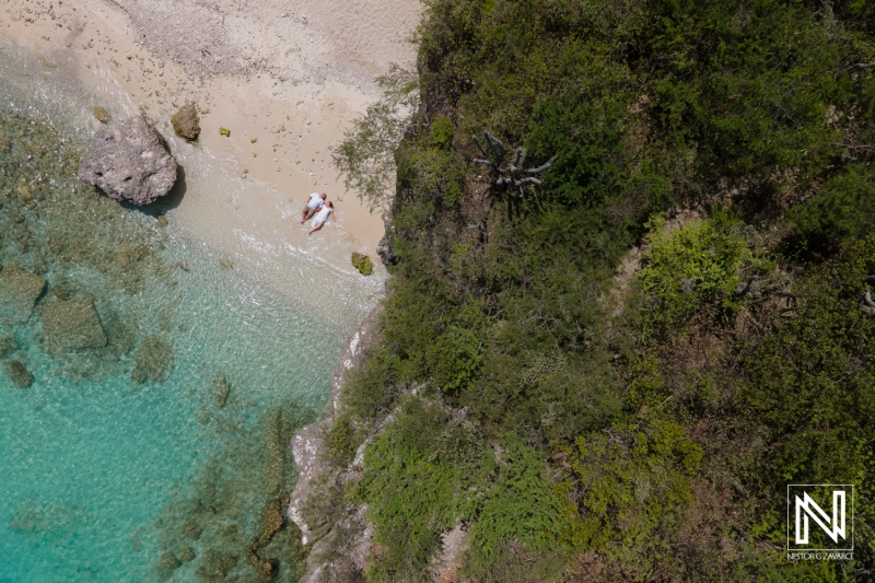 Aerial View of a Secluded Beach With Clear Turquoise Water and Lush Greenery During a Sunny Day, Showcasing Calm Waves Lapping at the Shore