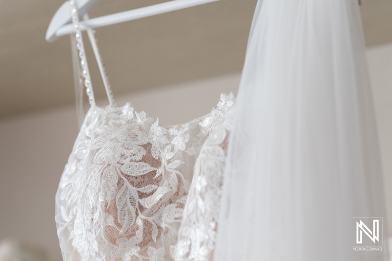 Elegant Bridal Gown Hanging on a Hanger, Showcasing Intricate Lace Details and Flowing Veil in a Softly Lit Preparation Area for the Wedding