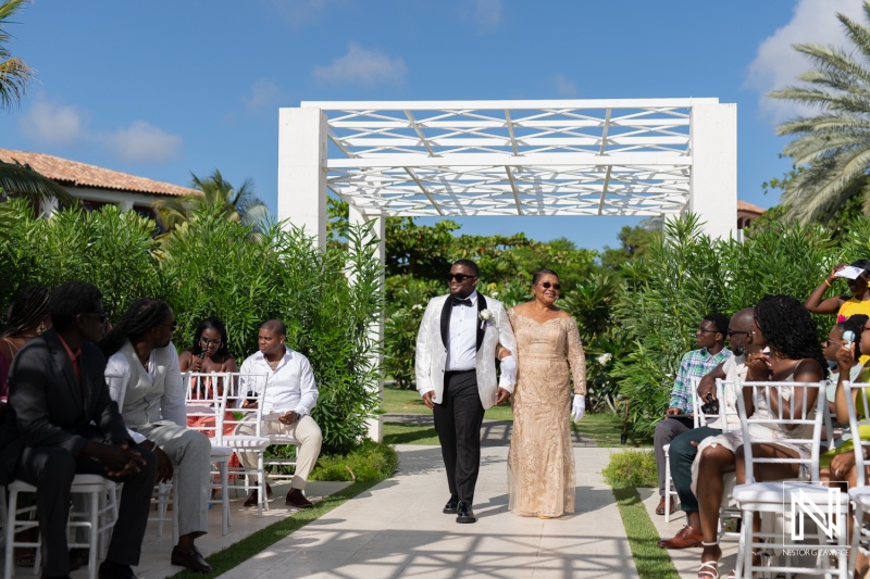 A Couple Walks Down a Beautifully Landscaped Aisle in a Tropical Garden During Their Wedding Ceremony, Surrounded by Family and Friends on a Sunny Afternoon