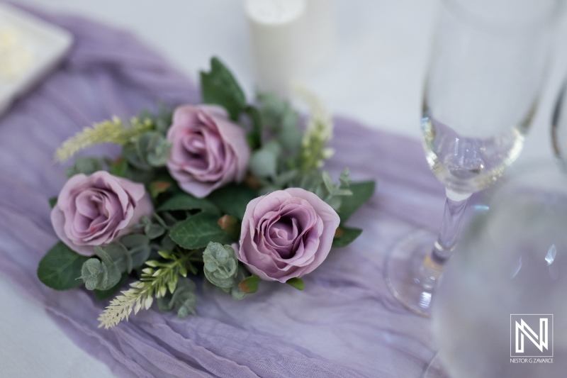 Elegant Table Arrangement Featuring Soft Lavender Roses and Greenery Placed Beside Champagne Flutes at an Indoor Event During the Evening