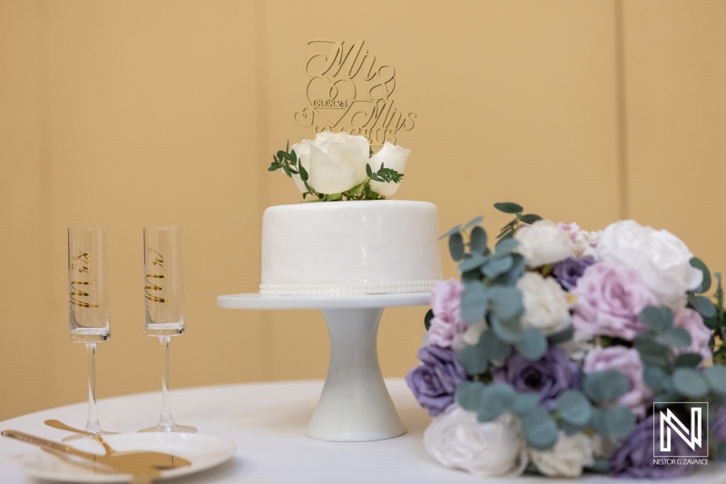 Elegant Wedding Cake Adorned With White Roses and a Decorative Topper Alongside Champagne Flutes and a Floral Bouquet on a Table Setting