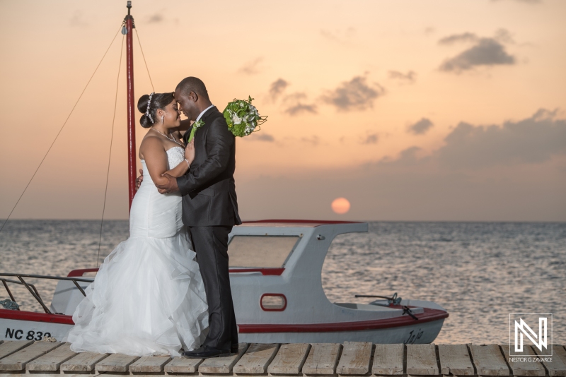 Bride and groom posing on the beach pier with a Curacao fisherman boat in the sunset