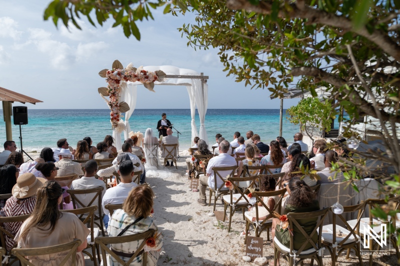 Wedding ceremony takes place at Playa Hunku in Curacao with guests seated near the beach in a sunny setting