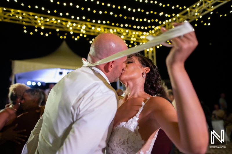 Couple shares a kiss during their wedding celebration at Playa Hunku in Curacao under string lights