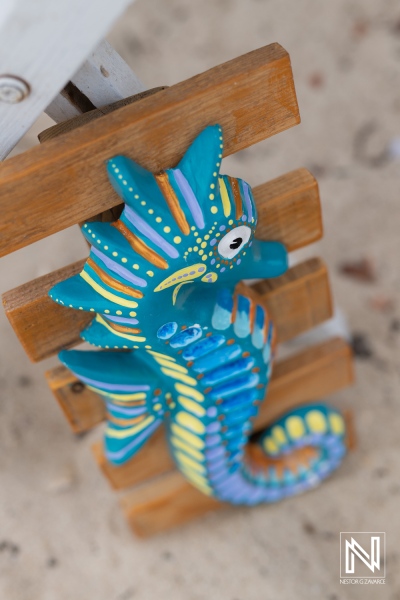 Colorful handcrafted seahorse decoration hanging on a wooden structure at a beachside location during a sunny day