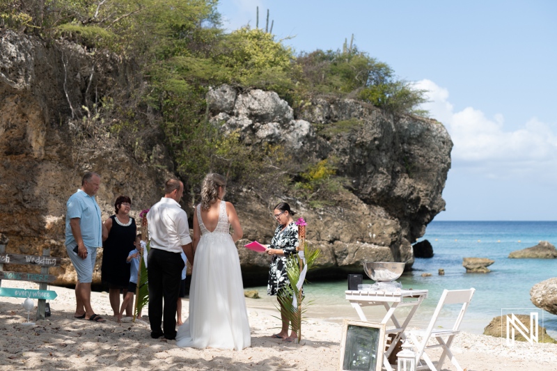 A beautiful beach wedding ceremony in a tropical paradise with a small group of guests gathering around the couple under a clear sky