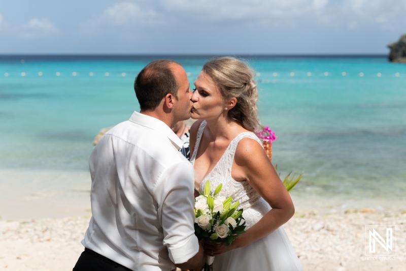 A couple shares a romantic kiss during their beach wedding ceremony in a tropical paradise with turquoise waters and soft white sand