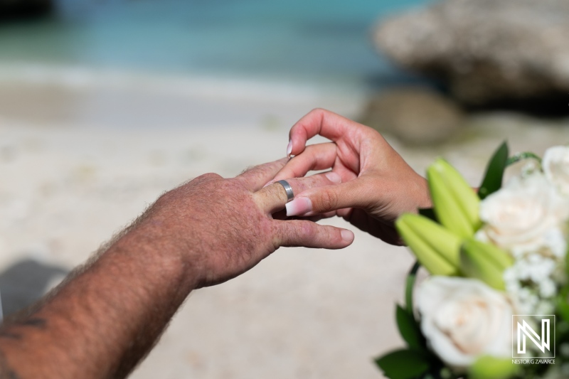 A couple exchanging wedding rings on a sandy beach with a beautiful ocean view during a sunny day, highlighting the moment of commitment and love