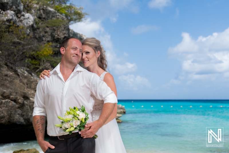 Couple celebrates their wedding at a beautiful beach location during a sunny day with turquoise waters and rocky cliffs in the background