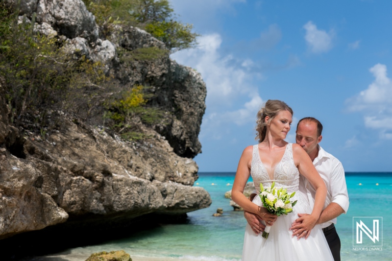 A couple enjoys a romantic moment on a beautiful beach with turquoise waters, rocky cliffs, and lush greenery during a sunny day