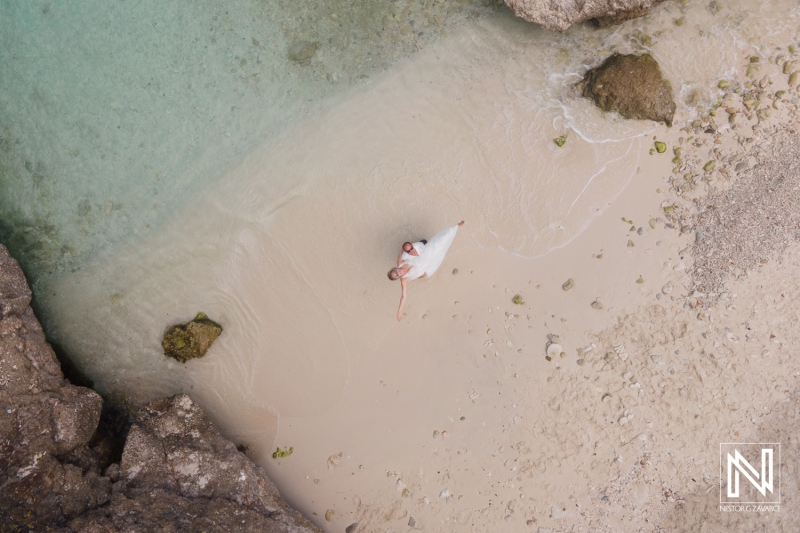 A bride with flowing veil stands gracefully on a sandy beach surrounded by clear turquoise waters during a sunny day captures a moment of romance before the wedding ceremony