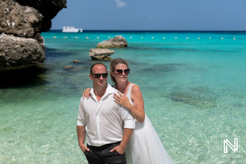 Couple enjoys romantic beach photoshoot in clear turquoise waters on a sunny day by the rocky shore celebrating their special occasion