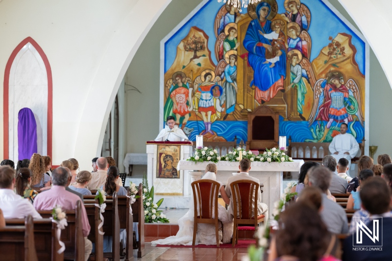 Couple exchanges vows during traditional Misa Di Jandoret wedding ceremony in Curacao surrounded by colorful altar art and family