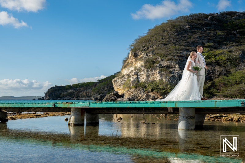 Beautiful wedding couple poses on wooden dock at Sint Michiel, Curacao, surrounded by stunning natural scenery and clear waters during the golden hour
