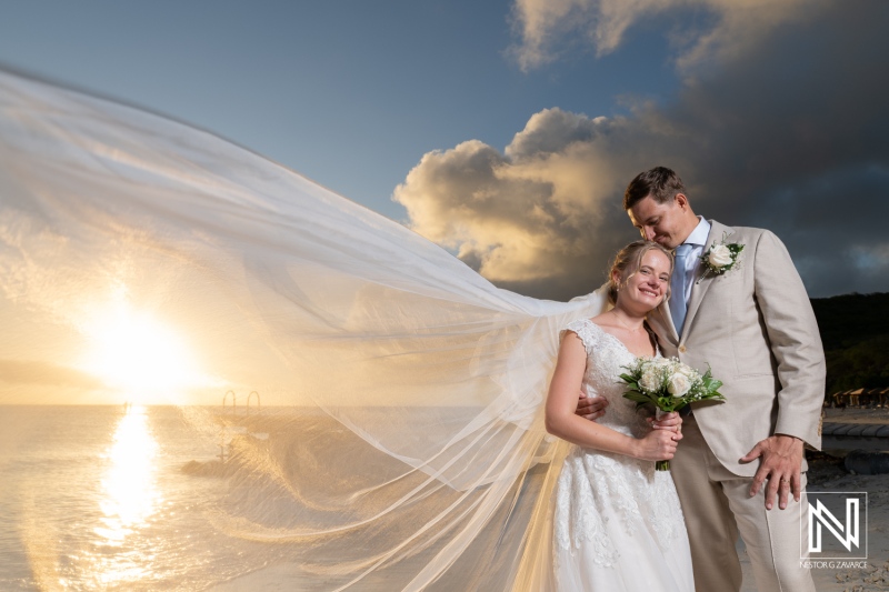 Wedding couple celebrates love at Playa Porto Mari in Curacao under a stunning sunset with a flowing veil