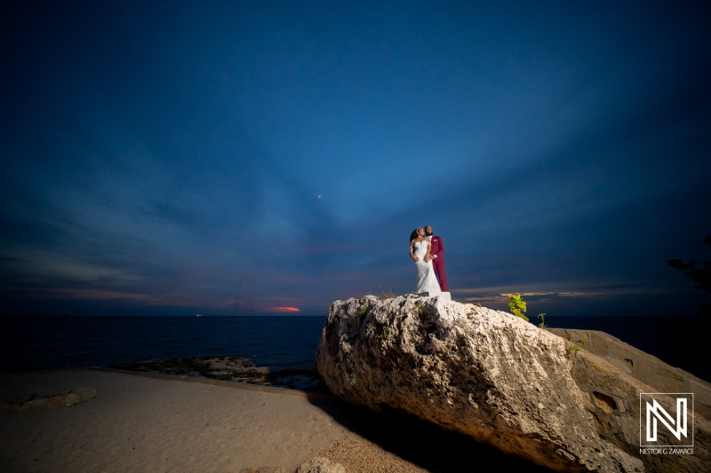 Couple stands on rock at wedding in Dreams Curacao Resort during sunset near the ocean