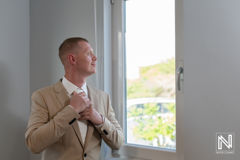 Groom adjusting his tie with a thoughtful expression in Curacao on his wedding day surrounded by bright light and serene atmosphere