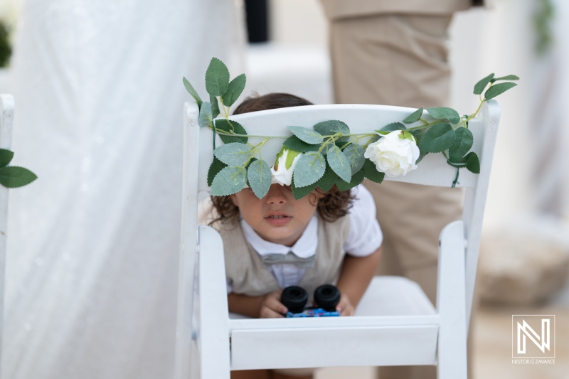 Child peeking through decorated wedding chair in Curacao while guests celebrate love on a sunny day