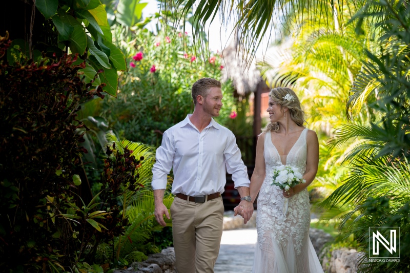 Couple walks hand in hand on their wedding day at Mood Beach in Curacao surrounded by tropical plants and flowers