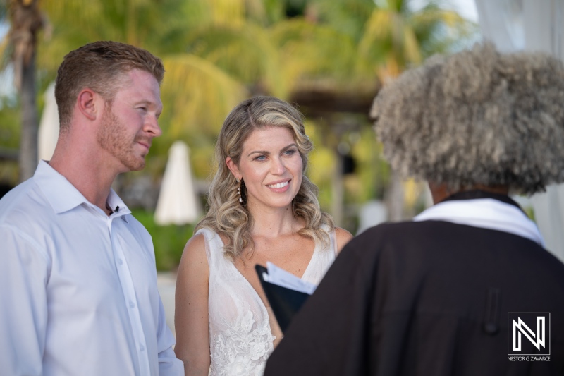 Couple exchanges vows during a wedding ceremony at Mood Beach in Curacao surrounded by guests on a sunny day