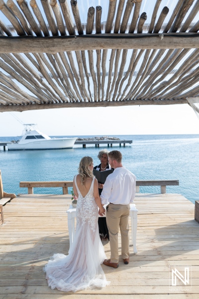 Couple exchanges vows on the waterfront at Mood Beach in Curacao during a wedding ceremony under a wooden structure