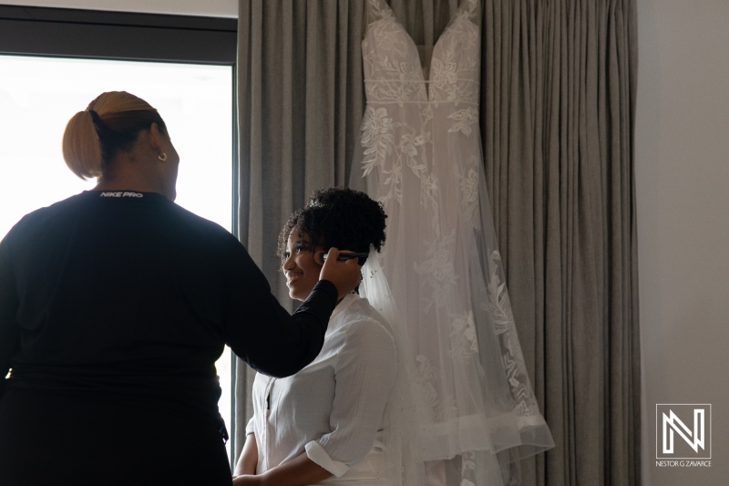 A Bride Prepares for Her Wedding Day While Getting Her Makeup Done in a Bright Room, With Her Wedding Dress Elegantly Displayed Behind Her