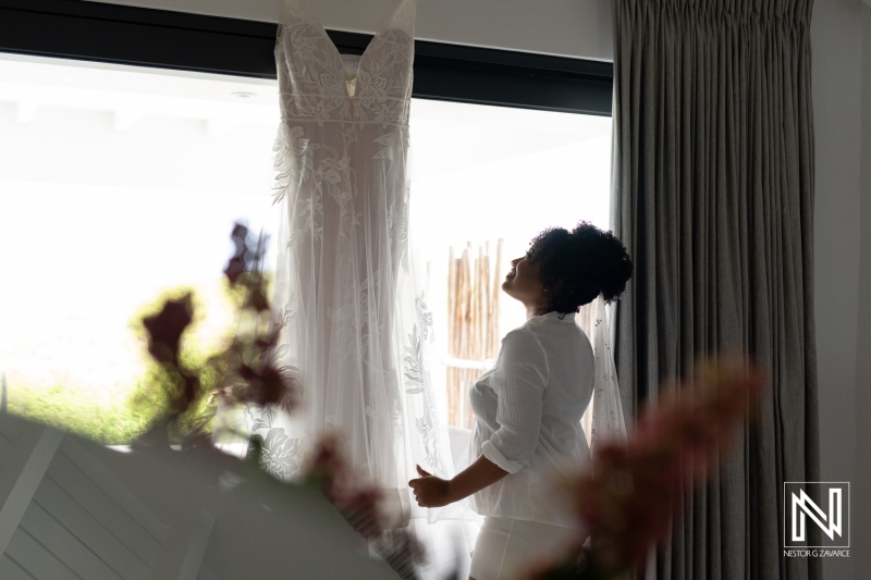 A Bride Admires Her Wedding Dress Hanging by the Window in a Modern Room Filled With Soft Natural Light During a Tranquil Morning