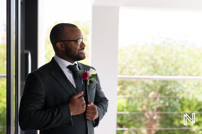 A Smiling Man in a Suit With a Rose Pinned to His Lapel Stands Confidently by a Large Window, Reflecting on a Meaningful Moment at a Formal Event