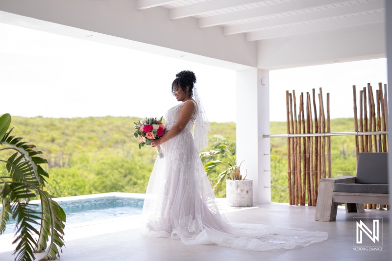 A Bride in a Stunning White Gown Stands by a Serene Poolside, Holding a Beautiful Bouquet, Surrounded by Lush Greenery in the Afternoon Light