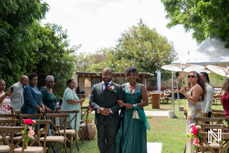 A Joyful Wedding Ceremony Unfolds Outdoors With Guests Seated at an Elegant Venue Under Vibrant Greenery and String Lights on a Sunny Day