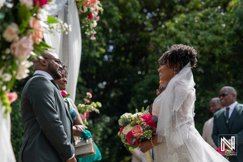 A Couple Exchanges Vows in a Serene Outdoor Setting Surrounded by Lush Greenery During a Joyful Wedding Ceremony Filled With Love and Beautiful Floral Arrangements