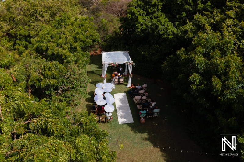 Aerial View of an Outdoor Wedding Setup Featuring a Canopy, Tables, and Chairs Among Lush Greenery on a Sunny Day