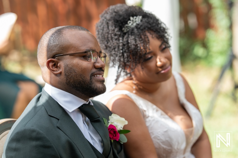 A Joyful Couple Smiling During Their Wedding Ceremony Outdoors, Surrounded by Lush Greenery and a Warm Afternoon Light, Capturing the Moment of Love and Connection