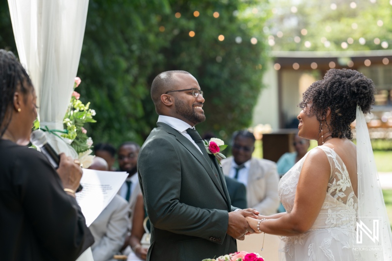 A Joyful Wedding Ceremony in a Lush Garden Setting With the Couple Exchanging Vows Under a Canopy Adorned With Flowers on a Sunny Day