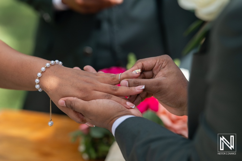 A Couple Exchanging Wedding Rings During an Outdoor Ceremony Surrounded by Floral Decorations in a Beautiful Garden on a Sunny Day