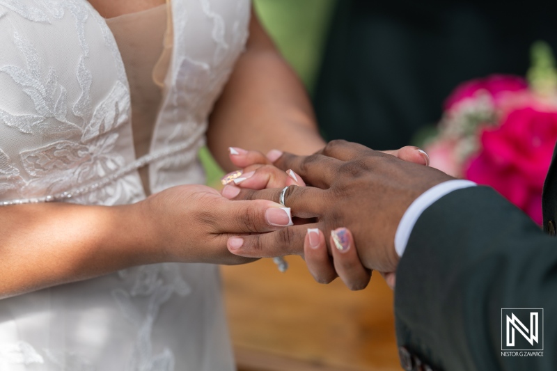 A Couple Exchanges Wedding Rings During Their Outdoor Ceremony Surrounded by Colorful Flowers and Greenery, Capturing a Moment of Love and Commitment