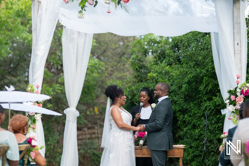 A Joyful Wedding Ceremony Held Outdoors With a Couple Exchanging Vows Under a Floral-Draped Arch Surrounded by Family and Friends in a Lush Garden Setting