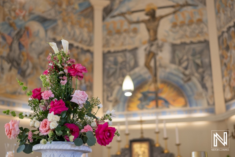 Floral Arrangement Adorned With Pink Roses in a Church Setting With a Striking Mural and Crucifix in the Background