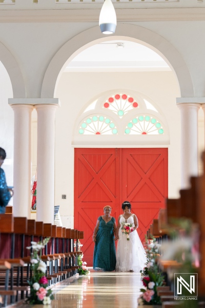 Bride and Bridesmaid Walking Down the Aisle of a Beautifully Decorated Church With Red Doors During a Wedding Ceremony