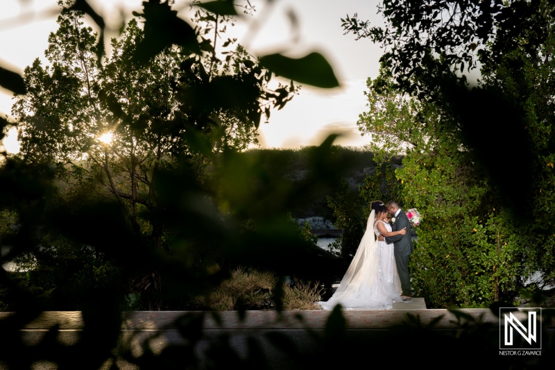 Couple Embraces During Their Wedding Ceremony at Sunset Surrounded by Lush Greenery in a Serene Outdoor Setting