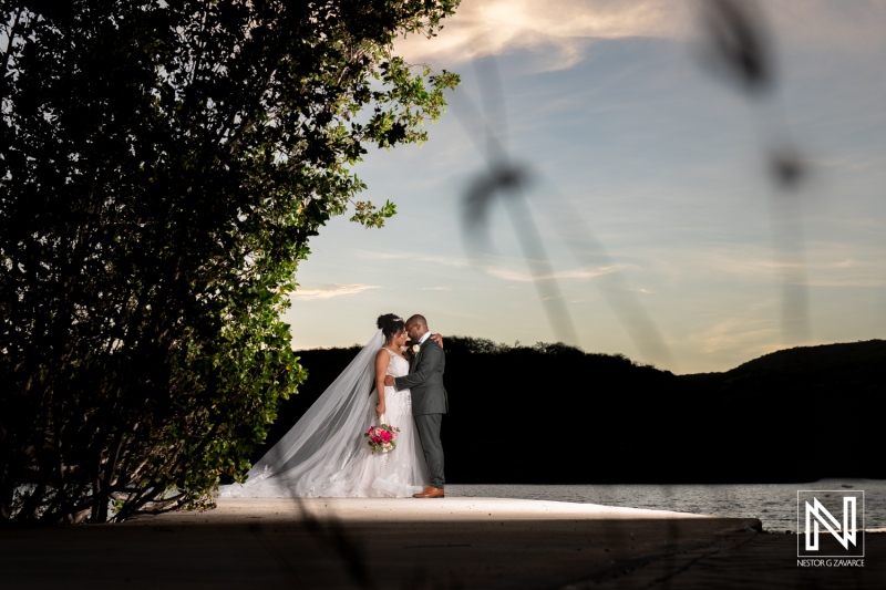 Couple Sharing an Intimate Moment by the Water During Sunset, Surrounded by Lush Greenery, Capturing the Essence of Love and Commitment at Their Wedding