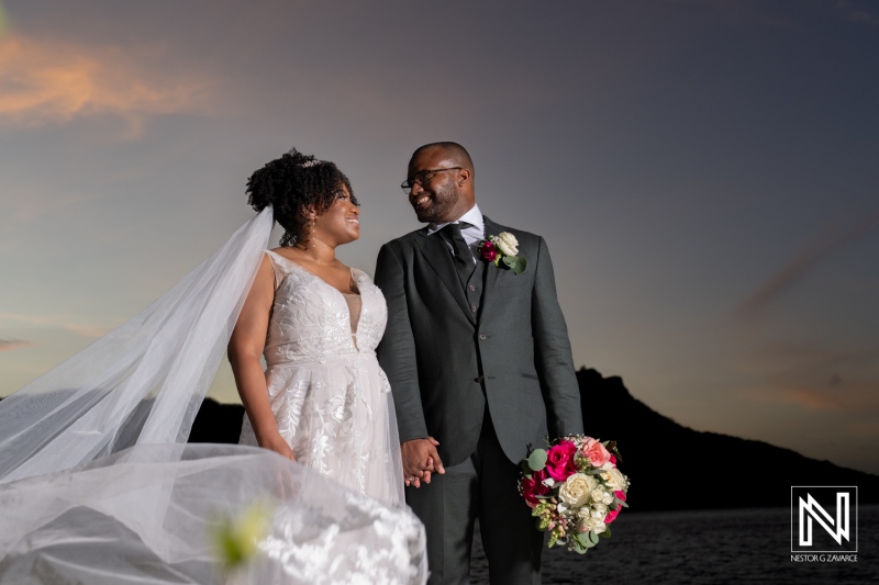 A Joyful Couple Shares a Romantic Moment at Sunset During Their Beach Wedding Ceremony With Scenic Mountains in the Background, Capturing Love and Happiness