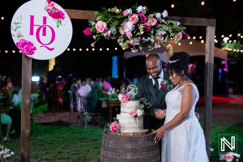 A Joyful Couple Shares an Intimate Moment as They Cut the Wedding Cake Outdoors Surrounded by Vibrant Decorations and Guests During a Festive Evening Celebration