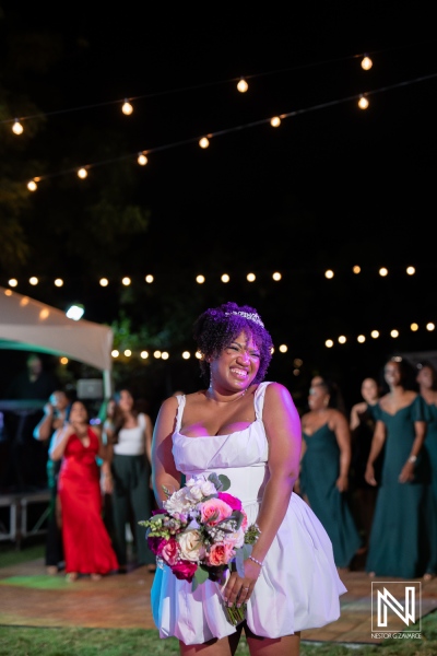 A Joyful Bride Celebrating During the Bouquet Toss at an Evening Wedding Reception Under String Lights in a Beautiful Outdoor Setting