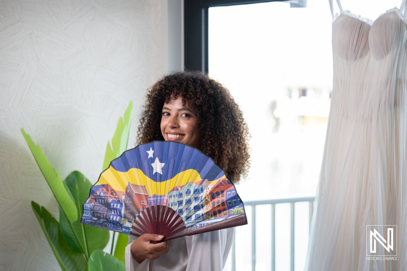 Wedding celebration at Avila Beach Hotel in Curacao with a bride holding a colorful fan and wedding dress in the background
