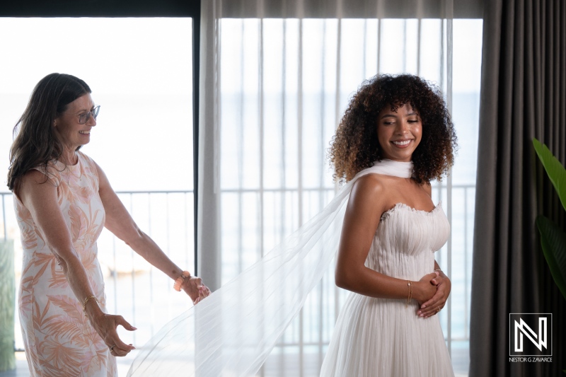 Bride prepares for wedding at Avila Beach Hotel in Curacao with the help of a friend as sunlight fills the room