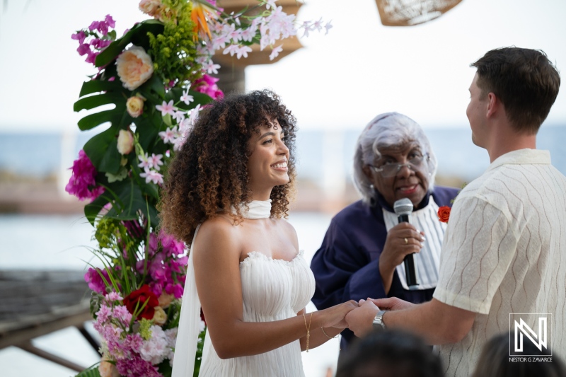 Couple exchanges vows in a wedding ceremony at Avila Beach Hotel in Curacao under colorful floral decorations