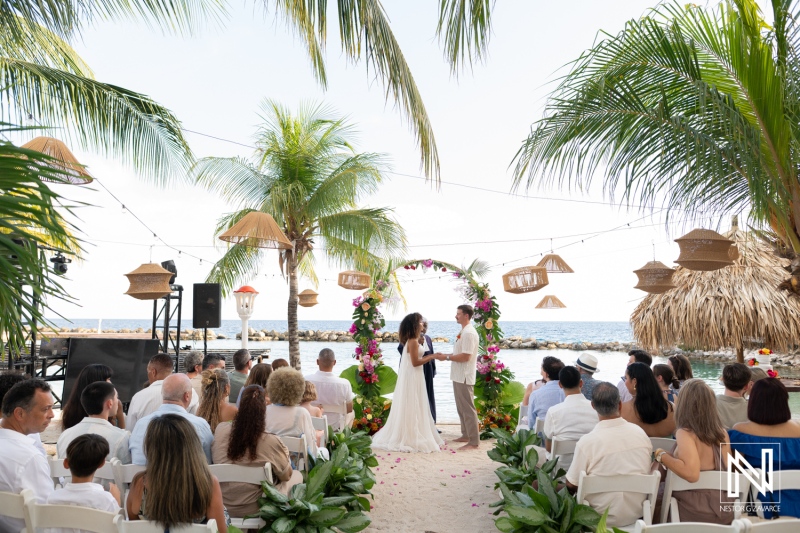 Wedding ceremony at Avila Beach Hotel in Curacao with guests in attendance by the ocean under palm trees